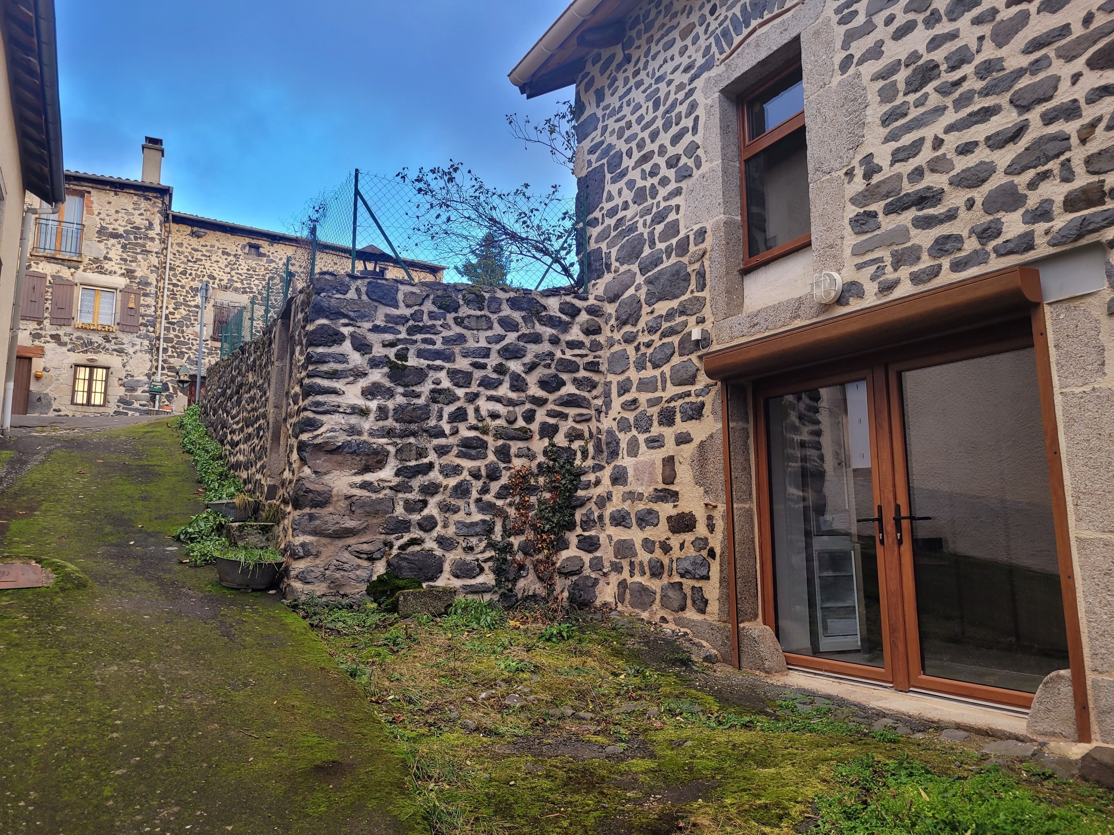 A stone building with a large window and a door, surrounded by a small garden area.