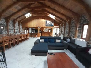 A spacious living area with a large sectional sofa, wooden dining chairs, a wooden coffee table, and a kitchen in the background.