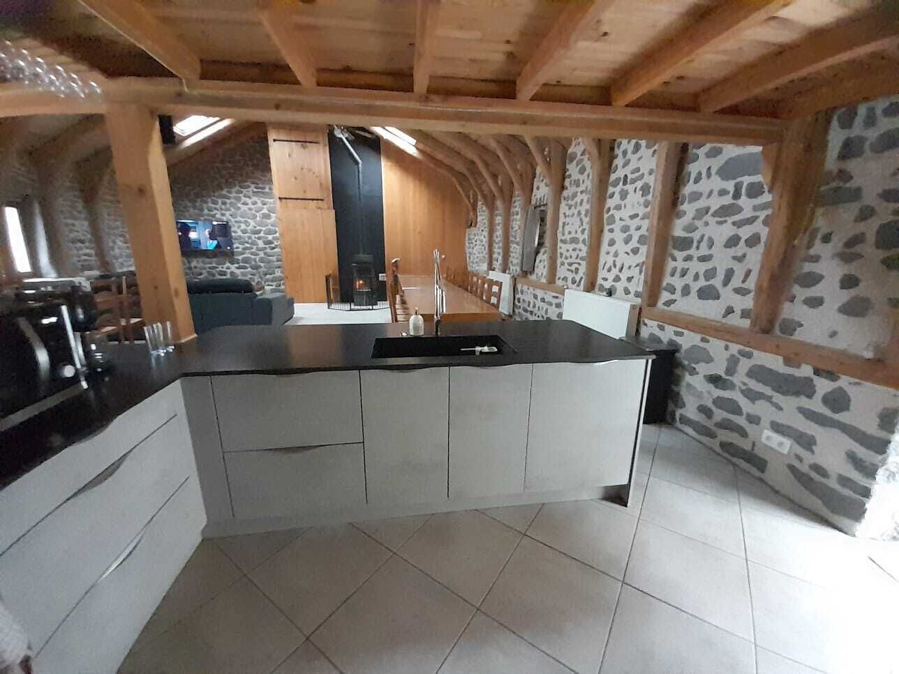 A kitchen with a central island, stone walls, and wooden beams.