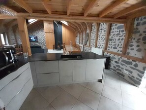 A kitchen with a central island, stone walls, and wooden beams.
