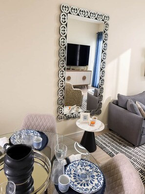 A modern living room with a round glass table, a sofa, a patterned armchair, and a decorative mirror with a unique frame. - Cana Life Luxury | City Beach Pool View Suite (Punta Cana)