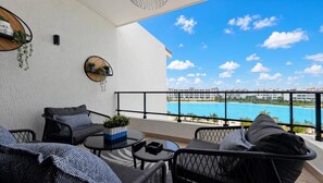 A balcony with outdoor furniture, a round table, and a view of a swimming pool and hotel buildings. - Cana Life Luxury | City Beach Pool View Suite (Punta Cana)
