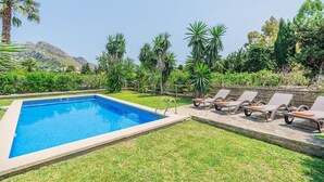 A swimming pool with a clear blue water, surrounded by a grassy area and a row of lounge chairs. - 2-bed Villa With Pool, Puerto Pollenca (Pollença)