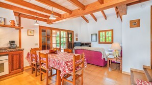 A cozy kitchen with wooden beams, a dining table set for four, and a kitchen counter with a coffee maker. - 2-bed Villa With Pool, Puerto Pollenca (Pollença)