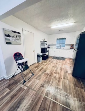 A compact kitchen with white cabinets, a black refrigerator, and a wooden floor. - Charming 3-Bedroom 2-Full Bath House in Alexandria (Alexandria)