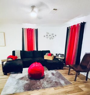 A living room with a black sofa, a red bean bag, a small table, and a chair.