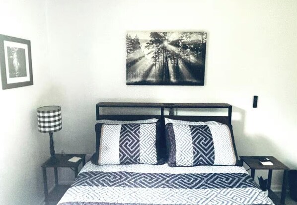 A bedroom with a bed, two nightstands, a lamp, and a wall-mounted picture.
