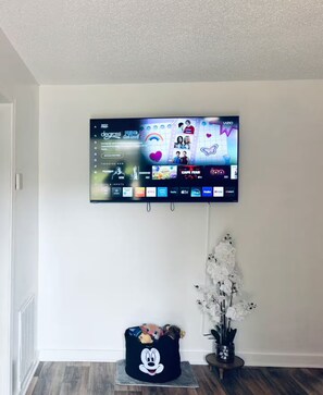 A flat-screen TV mounted on a white wall, displaying a streaming service interface with various content options. - Charming 3-Bedroom 2-Full Bath House in Alexandria (Alexandria)