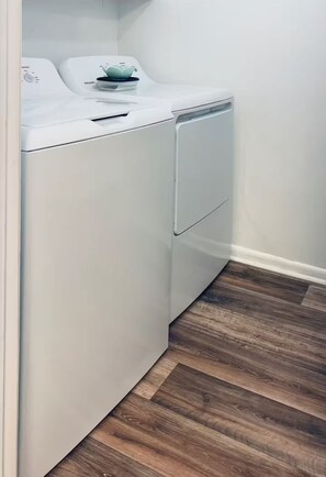 A compact, white laundry room with a built-in washer and dryer, wooden flooring, and a white wall.