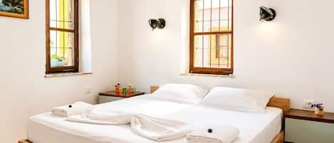 Un dormitorio con cama de madera, dos mesitas de noche, una lámpara de pared y un ventanal.