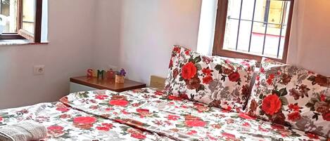 Et soveværelse med blomstret sengetæppe, et sengebord med lampe og et vindue med tremmer.