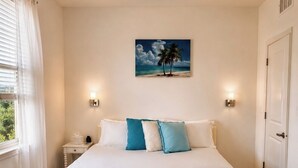 Un dormitorio con cama, ventilador de techo, pintura de una playa y mesita de noche con lámpara.