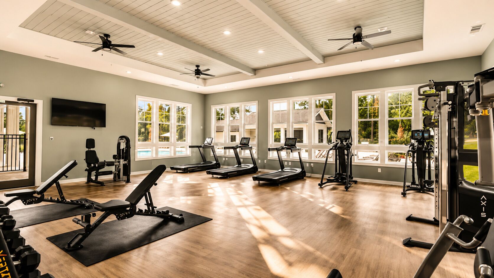 Une salle de sport équipée de tapis de course, d’appareils de musculation et d’un ventilateur au plafond.