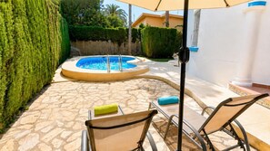 A swimming pool with a curved edge, surrounded by stone tiles and a wooden fence. There are two lounge chairs with cushions. - Villa Molins Aries - Three Bedroom Villa, Sleeps 6 (Les Marines)
