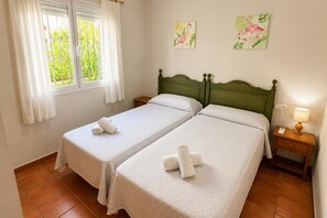 A hotel room with two single beds, a window with curtains, a bedside table with a lamp, and two wall art pieces. - Villa Molins Aries - Three Bedroom Villa, Sleeps 6 (Les Marines)