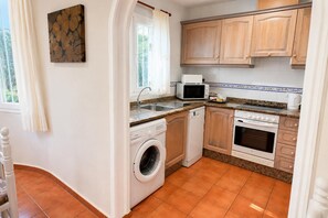A compact kitchen with a washing machine, microwave, oven, and a sink. - Villa Molins Aries - Three Bedroom Villa, Sleeps 6 (Les Marines)