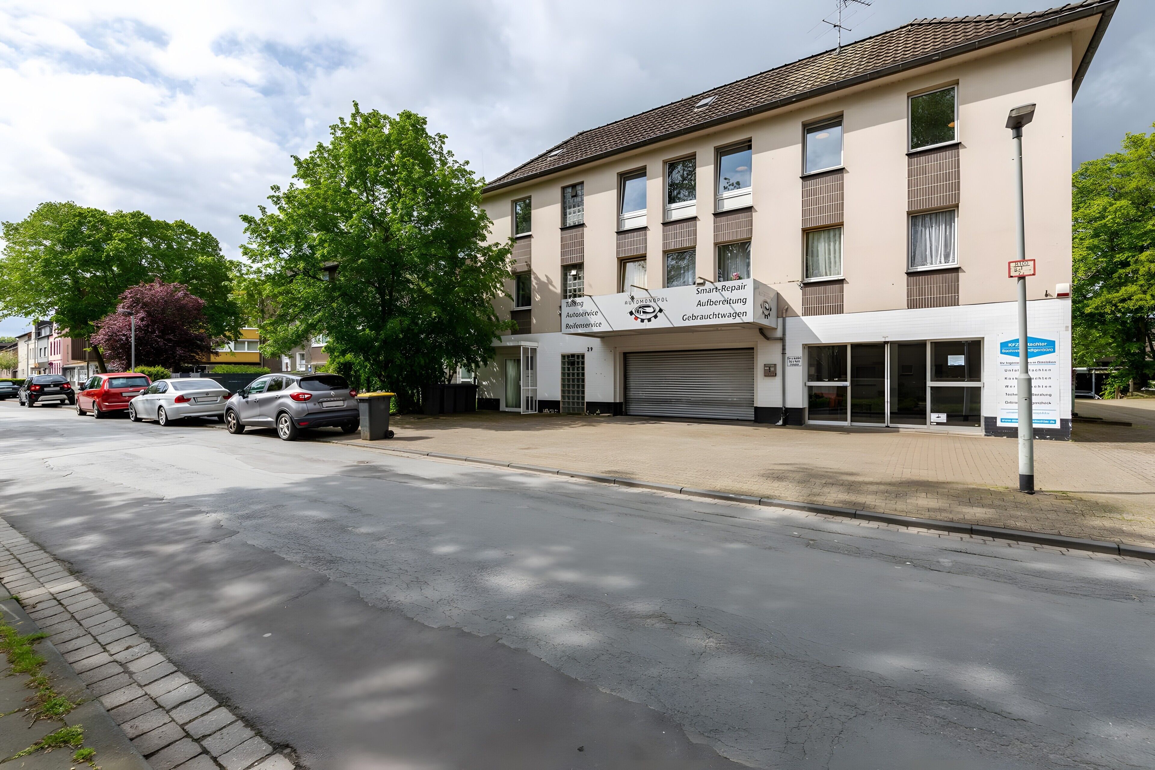 Ein mehrstöckiges Gebäude mit einer Garagenöffnung, geparkten Autos und einer Straße.
