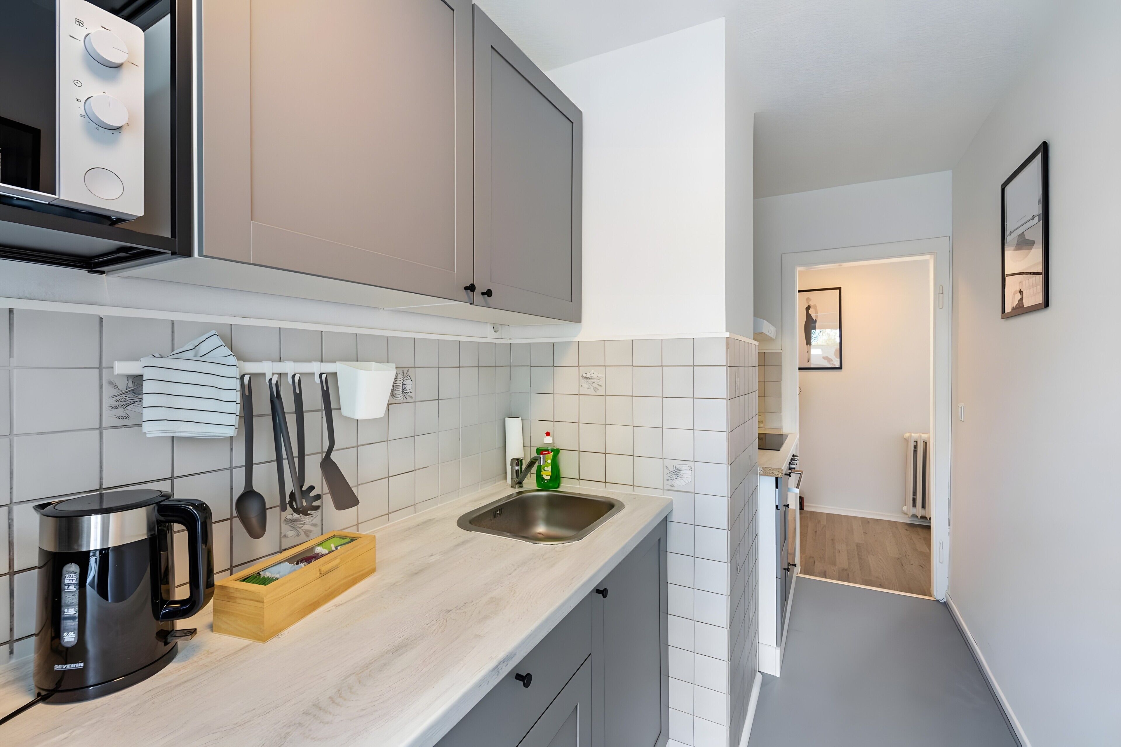 Een moderne keuken met grijze kastjes, een roestvrijstalen spoelbak en een waterkoker.