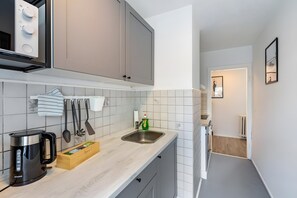 A modern kitchen with grey cabinets, a stainless steel sink, and a kettle.