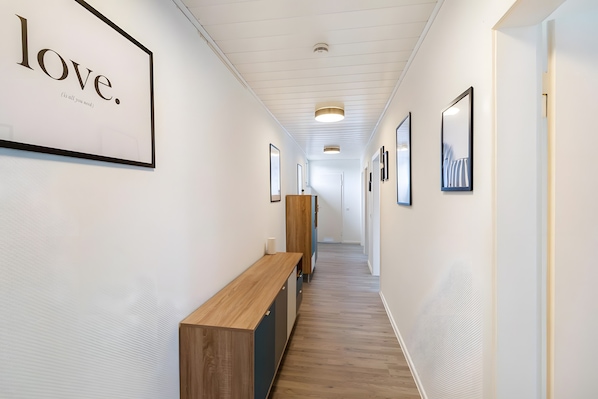 A hallway with framed artwork on the walls, a wooden bench, and a door at the end.