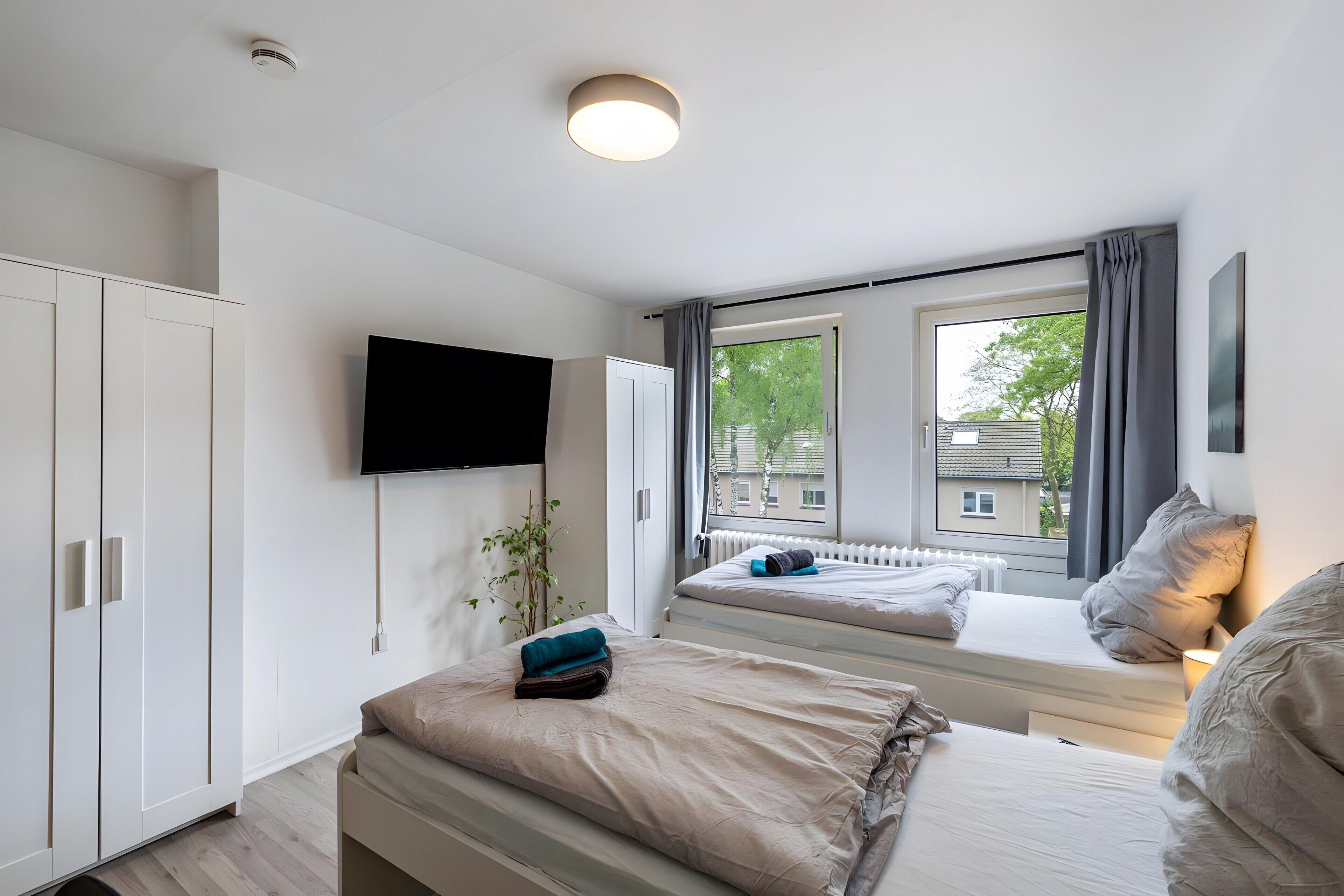 Ein modernes Schlafzimmer mit einem Bett, einem an der Wand montierten Fernseher und einem Fenster mit Vorhängen.