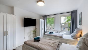 Ein modernes Schlafzimmer mit einem Bett, einem an der Wand montierten Fernseher und einem Fenster mit Vorhängen.
