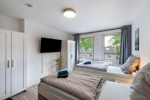A modern bedroom with a bed, a TV mounted on the wall, and a window with curtains.