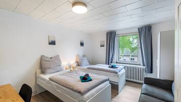 Una habitación con dos camas, una mesa de madera y un ventanal con cortinas.