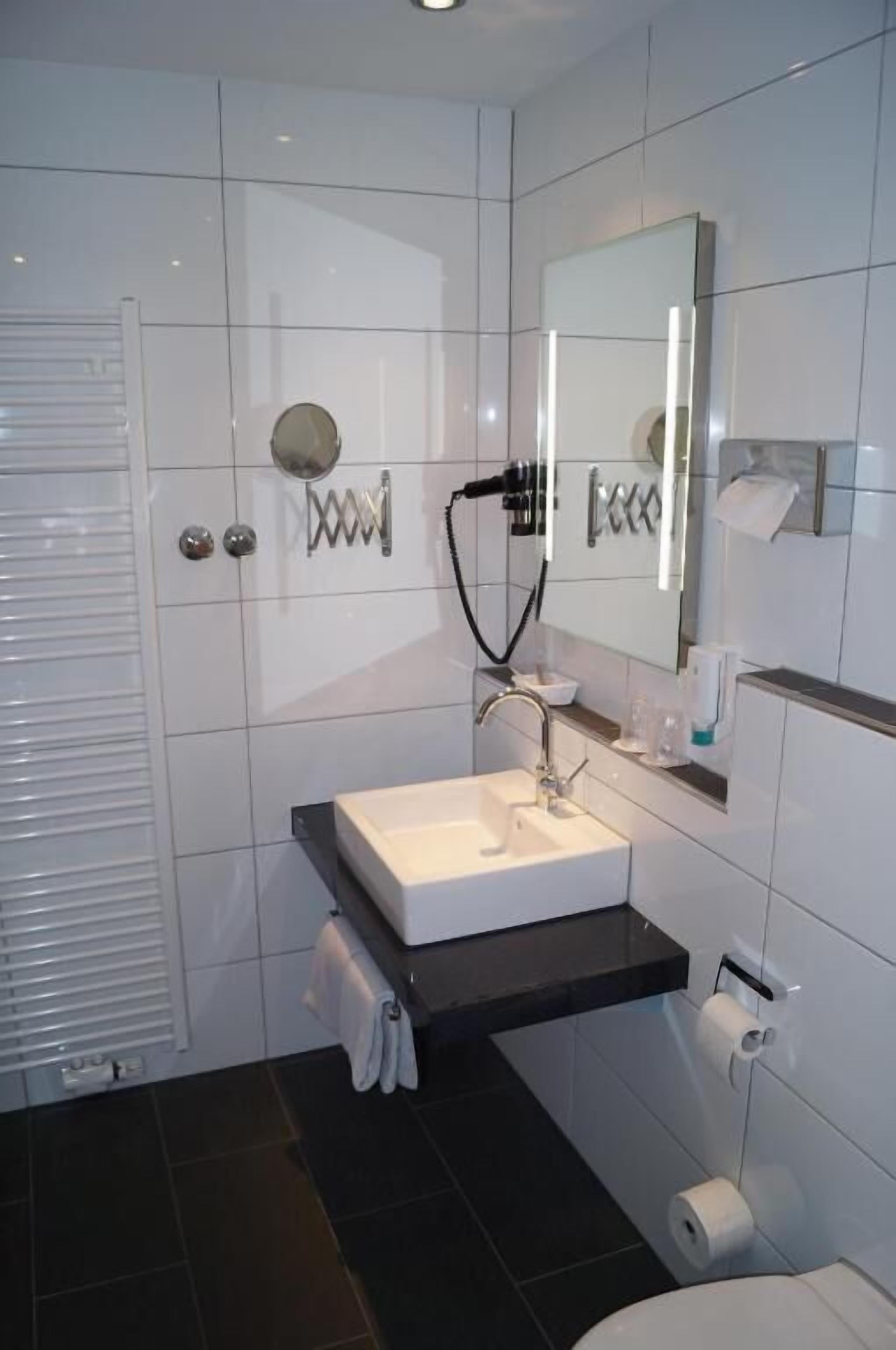 A modern bathroom with a white sink, a mirror, a towel rack, and a toilet.