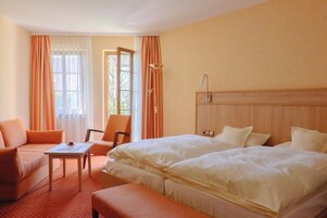 A hotel room with two beds, a sofa, a small table, and a chair.