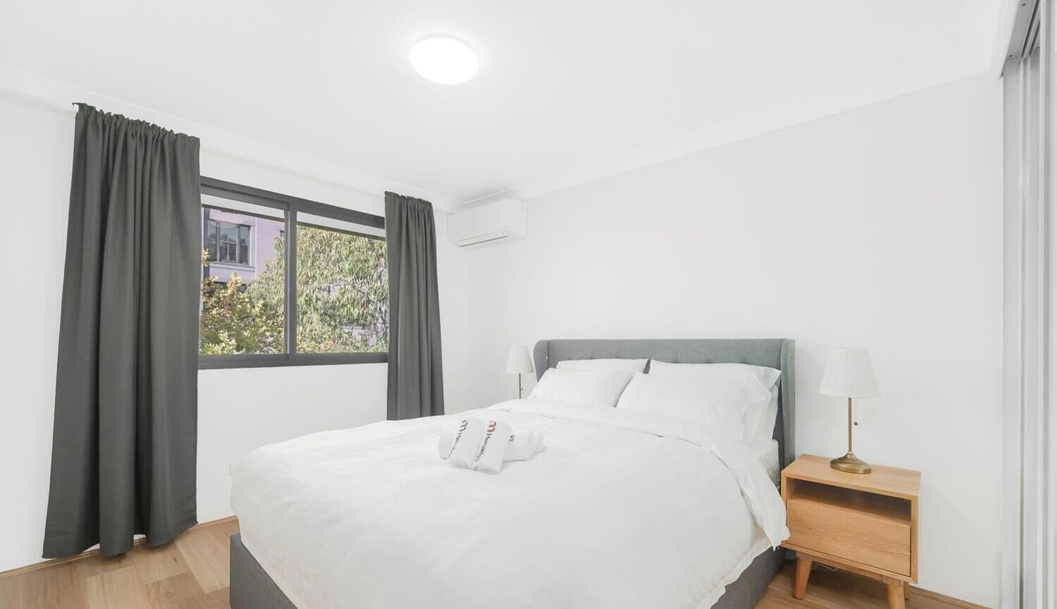 Habitación de hotel con cama, mesita de noche, lámpara y ventana con cortinas.