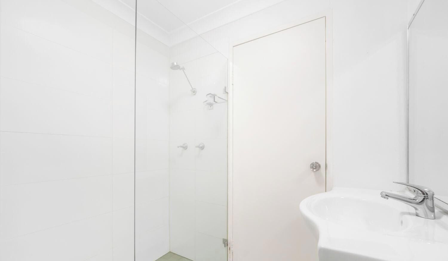 Een badkamer met een douchecabine van glas, een wit wastafelmeubel en een deur.