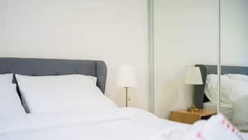 A neatly made bed with white bedding and a grey headboard, accompanied by a bedside table with a lamp.