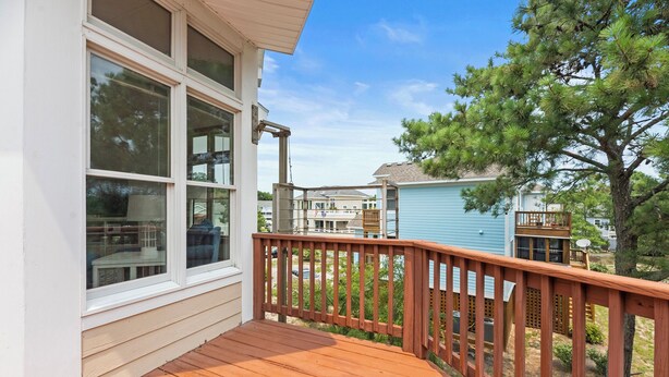 Eine Holzdar Terrasse mit Geländer, ein Fenster mit Rollläden und Blick auf benachbarte Häuser.