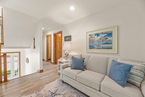 A living room with a sofa, a rug, a painting, and a lamp. - Dolphin's Cove: Dog Friendly | Hot Tub (Corolla)