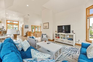 Ein geräumiges Wohnzimmer mit einem großen, blauen Sofa, einem weißen Couchtisch und einem Fernseher auf einem Holzboden.