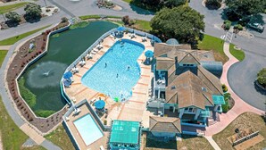 Ein Luftbild eines Wohngebiets mit einem großen Schwimmbad, einem Tennisplatz und einem Haus mit einem außergewöhnlichen Dachdesign.