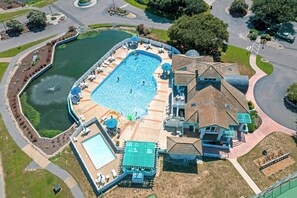 Ein Luftbild eines Wohngebiets mit einem großen Schwimmbad, einem Tennisplatz und einem Haus mit einem außergewöhnlichen Dachdesign.