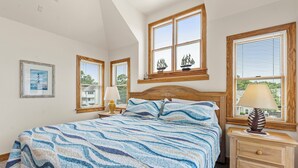 Ein Schlafzimmer mit Bett, Nachttischen, einem Fenster mit Blick und einem gerahmten Bild an der Wand.