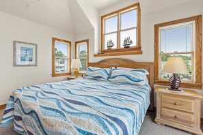 Ein Schlafzimmer mit Bett, Nachttischen, einem Fenster mit Blick und einem gerahmten Bild an der Wand.