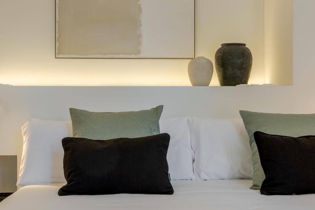 A bed with white and green pillows, a vase, and a painting on the wall.