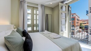 Habitación de hotel con cama, almohadas, ventana con cortinas y vistas a la ciudad.