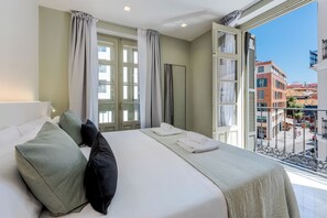 Habitación de hotel con cama, almohadas, ventana con cortinas y vistas a la ciudad.