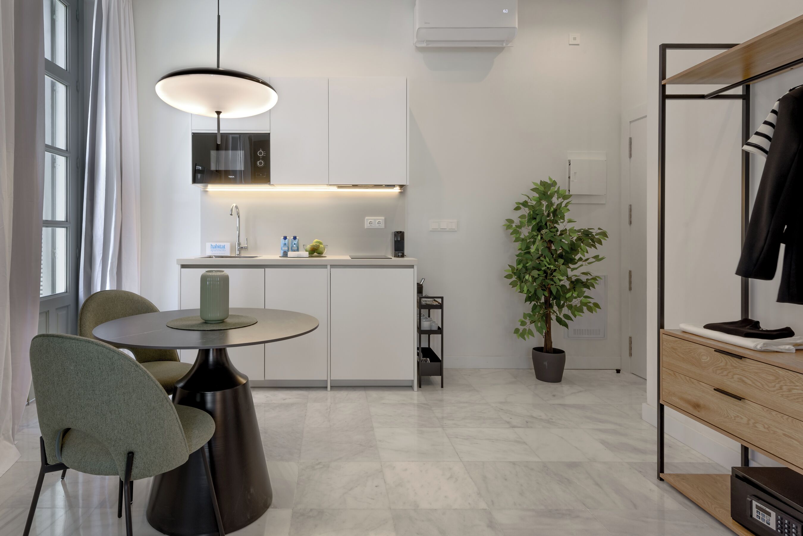 A modern kitchen with a central island, a dining area with chairs, a pendant light, and a potted plant.