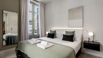 Una habitación de hotel con cama, mesita de noche, espejo y ventana con cortinas.