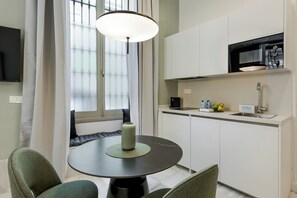 A modern kitchen with a dining area, including a round table with chairs, a hanging light fixture, and a window with curtains.