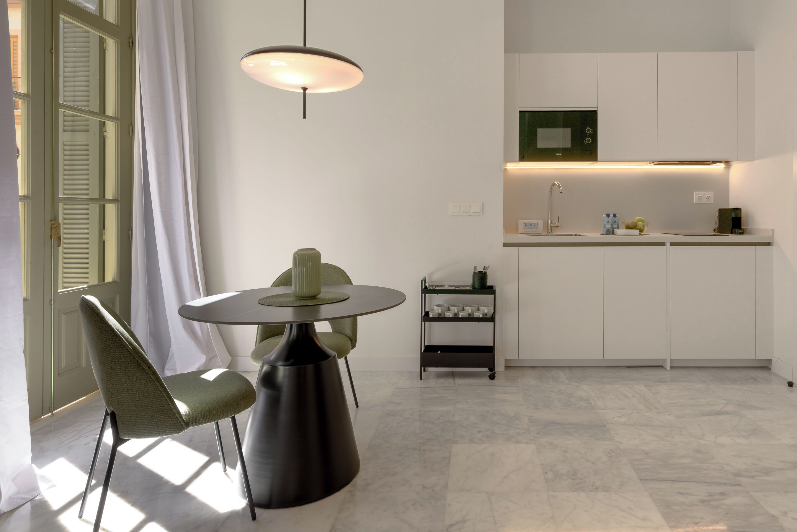A modern kitchen with a microwave, a sink, and a small countertop. There is a dining area with a table and chairs.