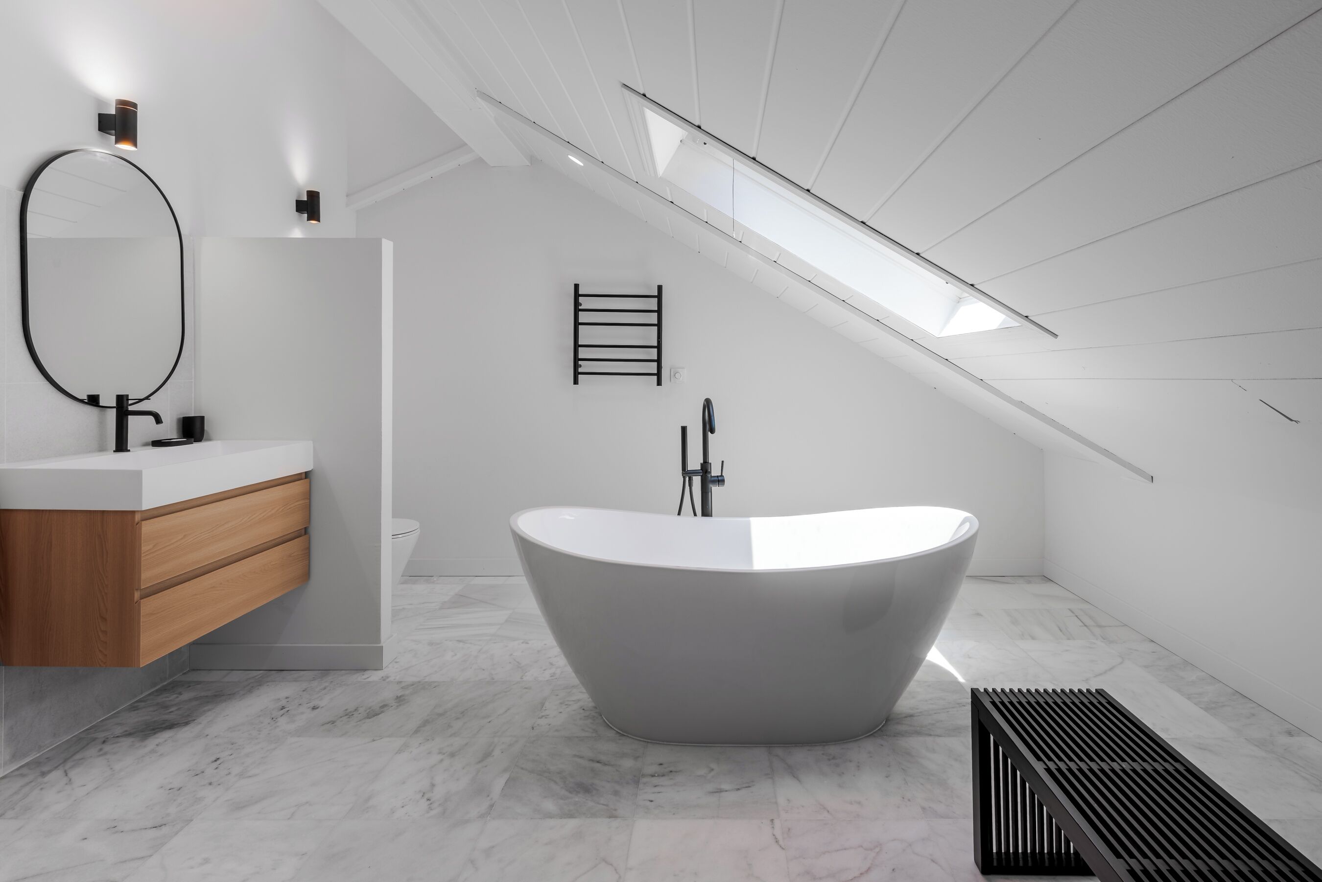 Un baño moderno con una bañera independiente, un tocador con espejo y un tragaluz.