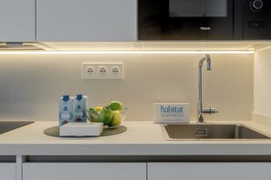 Una cocina moderna con microondas integrado, un lavamanos de acero inoxidable y un cartel de kit de limpieza.