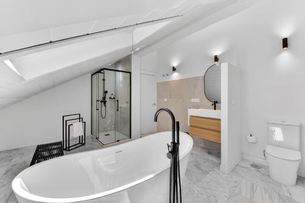 Ein modernes Badezimmer mit einer freistehenden Badewanne, einer einteiligen Glasdusche und einem hölzernen Waschtisch.